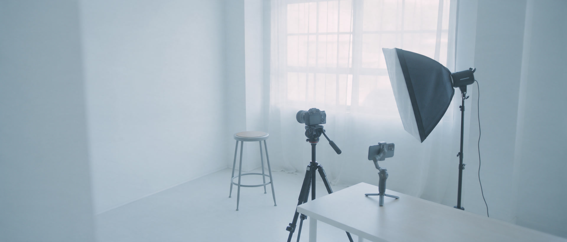 A small content studio corner with a camera on a tripod, a softbox light and a phone on a gimbal.